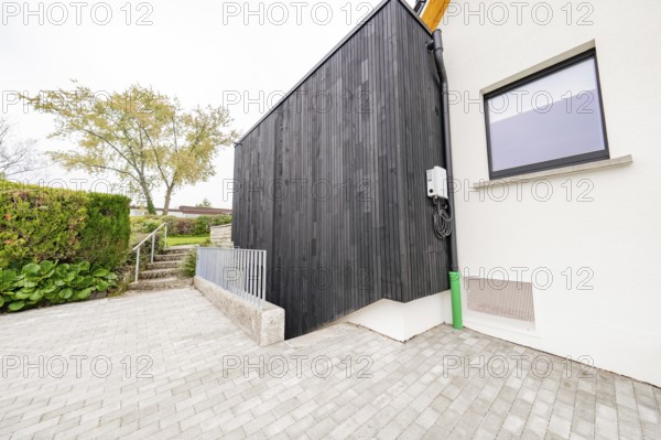 Modern house side with black wood paneling on paved driveway, house renovation, air conditioning