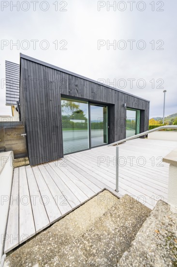 Terrace with wooden deck and glass front, access via ramp with metal handrail, clear modern lines