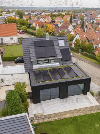 Aerial view of a modern single-family house with solar systems on a gable roof and green extension