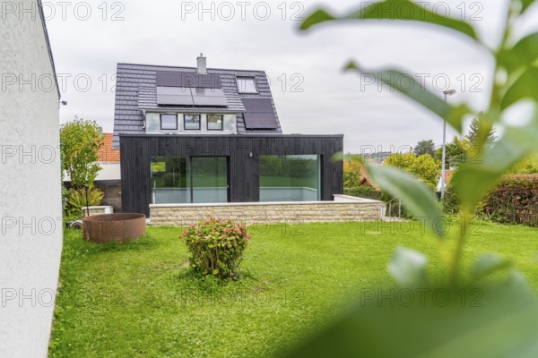 Modern extension with glass front on a green garden, framed by leaves in the foreground, quiet