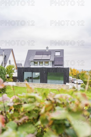 Residential building with black extension and glass front between neighboring houses, autumnal