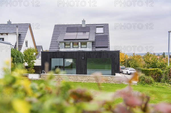 House with solar panels and black extension, view over garden to quiet street with parked car,