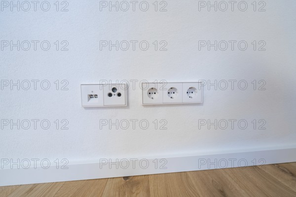 Modern sockets and connections neatly integrated into a white wall over oak floors, house