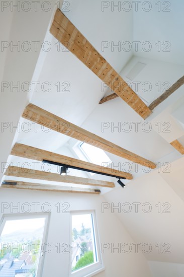 View of ceiling beams with skylight and rail spot in a bright attic room, house renovation, climate