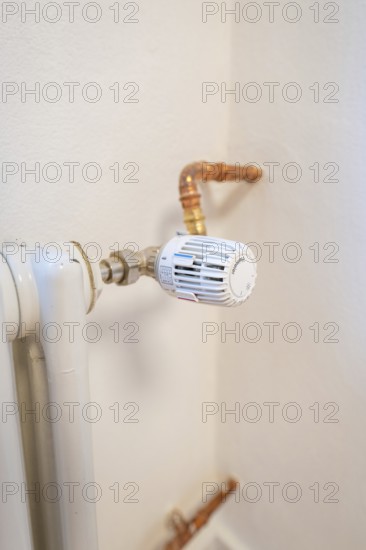 Detail of a radiator thermostat with copper lines on a white wall, house renovation, climate
