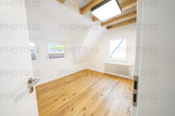Light-flooded attic room with oak floors and visible beams, freshly renovated and minimalistic