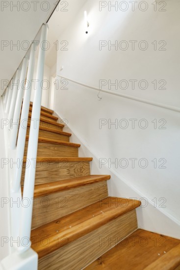 Wooden staircase with white railing and wall lamp in bright, simple staircase, house renovation,
