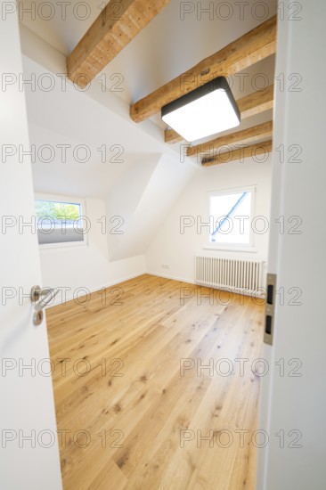 Bright attic room with oak floor and visible beams, viewed through the open door, house renovation,