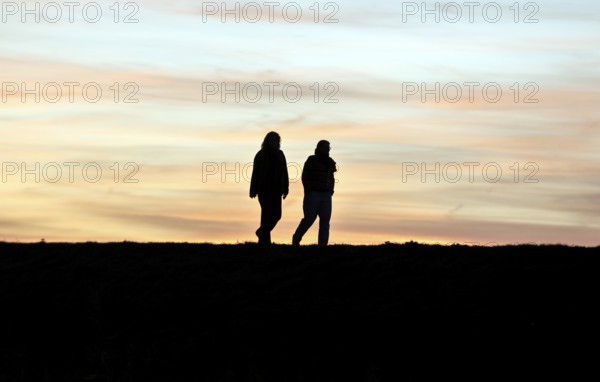 Walkers walk across a dike at sunset, Fehmarn Island, 13.10.2025, Fehmarn, Schleswig-Holstein,