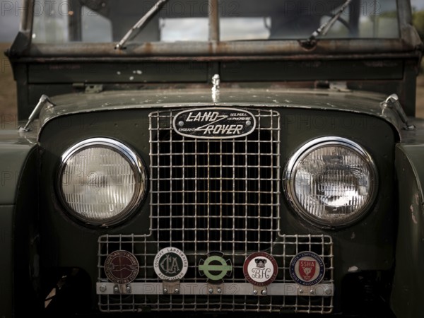 The front end of a 1950's Series One Land Rover, adorned with hunt club badges on the front grill,