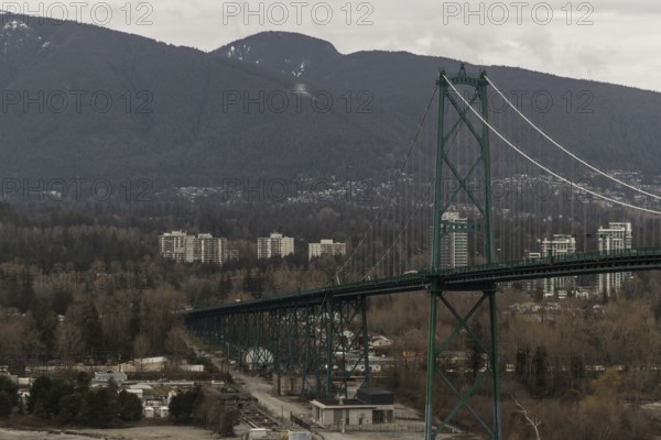 A long suspension bridge connecting a cityscape with mountainous surroundings under an overcast sky