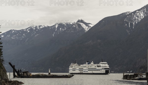 A ferry cruises through a scenic region with snowy mountains and cloudy skies in Horseshoe Bay,