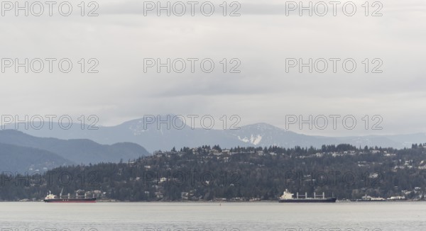 Distant view of ships passing by mountain-lined shores under cloudy skies in Vancouver, British