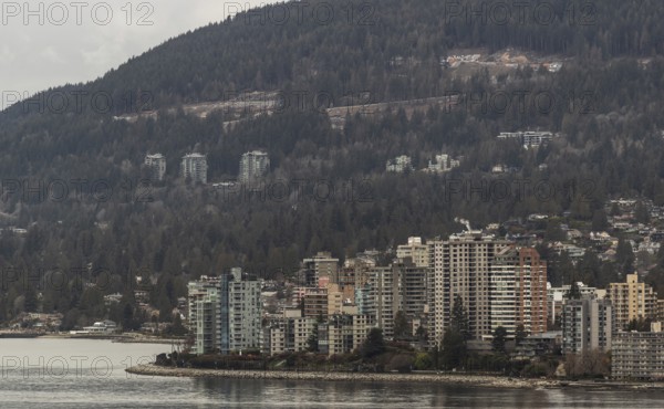 Urban high-rise buildings set against a backdrop of forest and mountains on an overcast day in