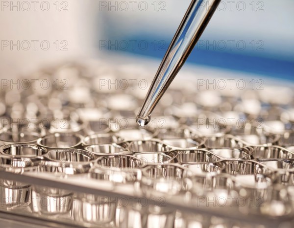 Reflective wells shimmer as a pipette releases a precise droplet, Pipette dispensing a liquid onto