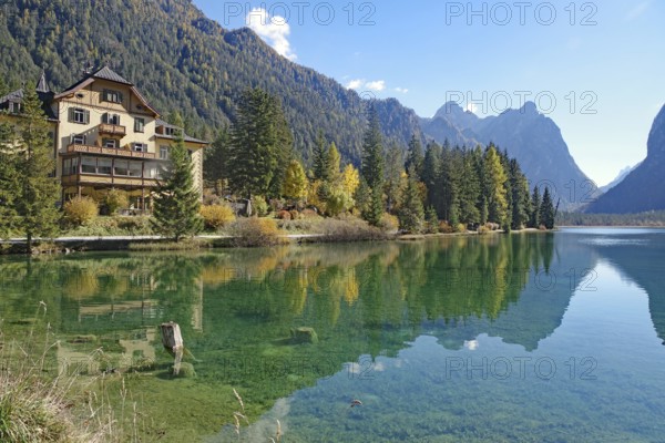 Waterfront villa on a clear mountain lake reflected against rugged peaks, sunny autumn colors glow