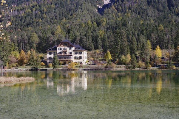 The villa is brilliantly reflected in a quiet alpine lake in front of dense forest and gentle