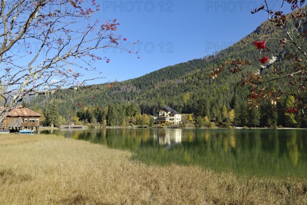 Autumnal alpine lake with clear water, a lakeside hut and red berry branches frame the view of the