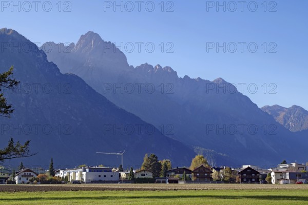 Village at the foot of rugged mountains, wide meadow in the foreground, clear air and soft light,