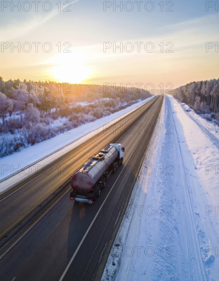 Petrol cargo truck lorry tanker driving on highway hauling oil products at sunrise, wide snowy