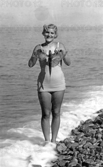 Woman on the beach in a bathing suit with flying fish, presumably swallowfish (Exocoetus volitans),