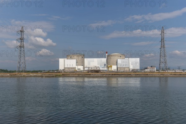 A large industrial nuclear power plant is located on a quiet water front. Two tall cylindrical