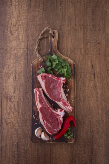 Freshly sliced lamb chops, with herbs and vegetables, on a wooden board, ready to cook, on a wooden