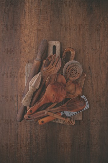 A variety of wooden kitchen utensils are arranged on a dark brown wooden surface. Items include