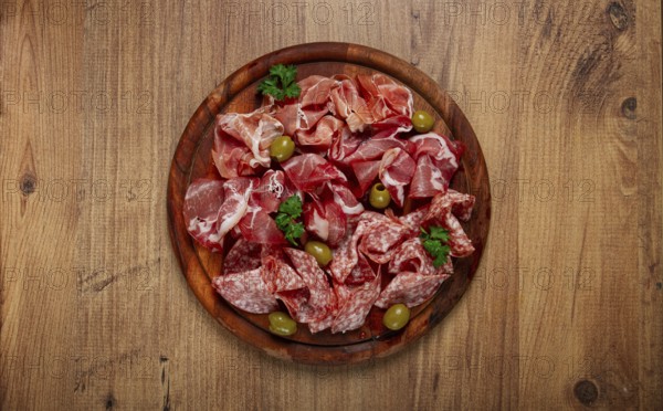 Assortment, sliced meat appetizer, prosciutto, salami and ham, with olives, on a wooden board,