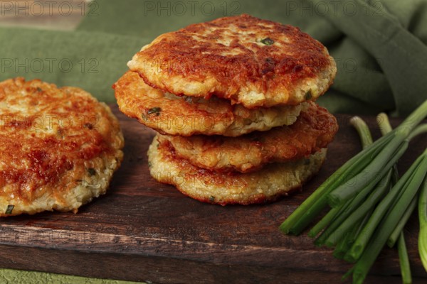 Crispy potato pancakes Latkes, stacked on a wooden board next to fresh green onions, natural light,