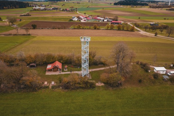 View of an observation tower in a rural area with fields and a village in the background,
