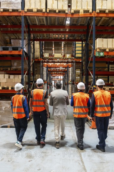 Diverse team of manager and warehouse workers in safety vests and hard hats walking through a