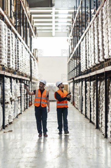 Warehouse workers in high visibility vests and hard hats checking inventory and managing logistics
