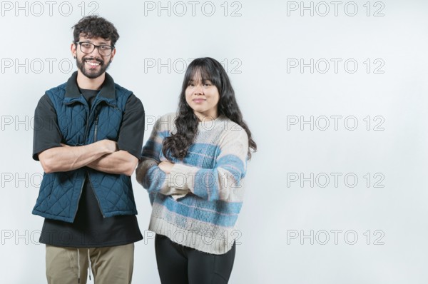 Smiling young couple with crossed arms looking at camera, isolated. Cheerful young multiethnic