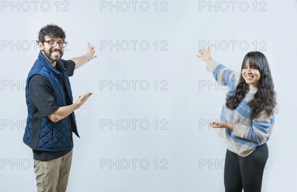 Happy couple showing something and smiling at the camera, isolated. Young couple presenting