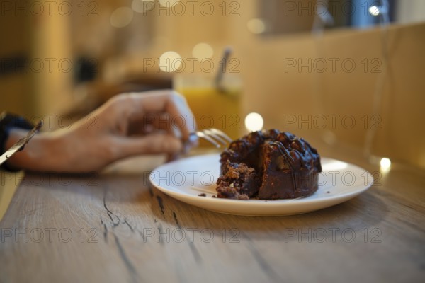 A hand reaches for a fork to savor a piece of rich chocolate dessert on a plate. Soft lighting