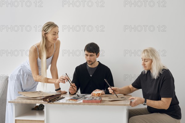Three friends gather around a table, engaged in artistic activities. One friend takes the lead