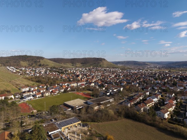 Large-scale city view with sports field in the foreground, surrounded by hills and blue skies, Korb