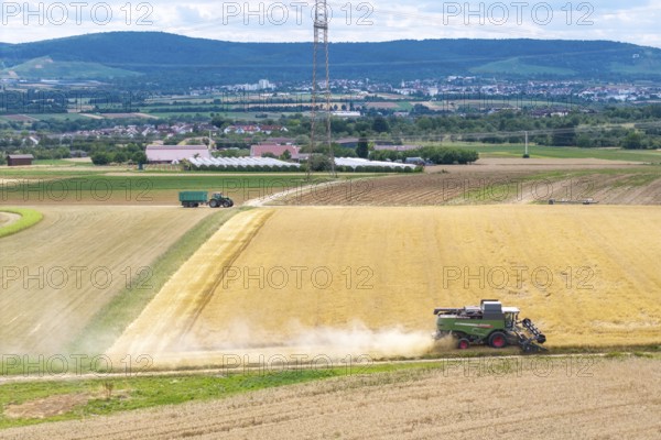 Harvester works in vast fields, clear view of adjacent landscape due to sunny weather, Mähresc Korb
