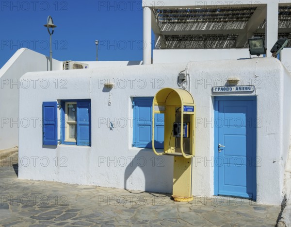 Mykonos, Cyclades, Greece - Old yellow telephone box in front of white house with blue shutters in