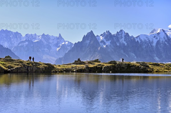 A group of hikers at Lac de Chésserys, behind the snow-covered Mont Blanc massif,