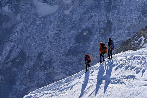 Three ascended mountaineers run across a snow-covered mountain ridge, Aiguille du Midi,