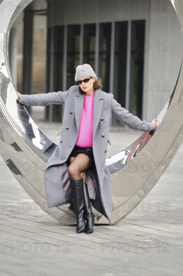A woman poses confidently in an urban environment, showcasing vibrant clothing against contemporary