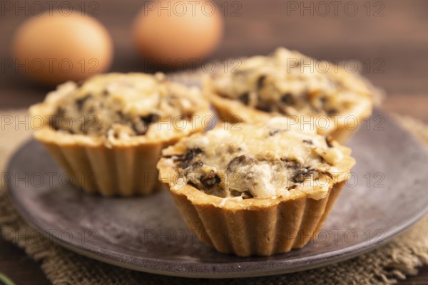 Tartlets with meat and cheese on brown wooden background and linen textile. side view, close up,