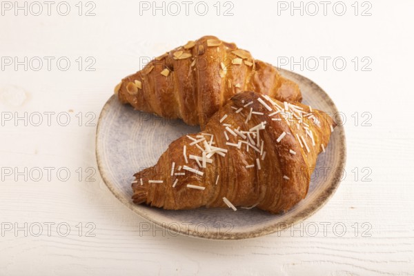 Croissant on blue plate on white wooden background, side view, copy space