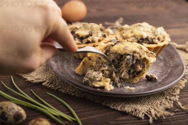 Tartlets with meat and cheese with hand on brown wooden background and linen textile. side view,