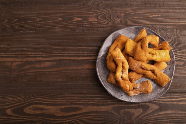 Crunchy biscuit Brushwood cookies sprinkled with powdered sugar on brown wooden background, top