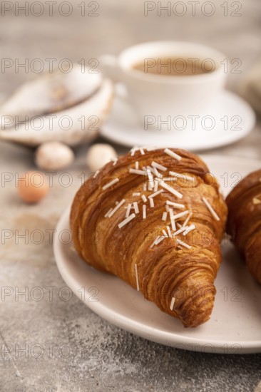 Croissant on white plate on brown concrete background and linen textile, cup of coffee, side view,