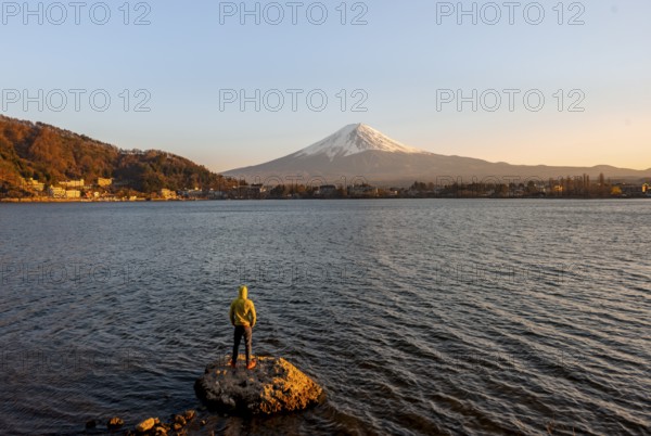 Young man standing on rocks in Lake Kawaguchi, view of Mount Fuji volcano at sunset, Yamanashi
