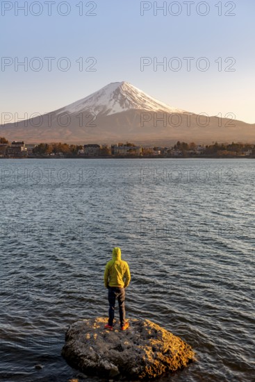 Young man standing on rocks in Lake Kawaguchi, view of Mount Fuji volcano at sunset, Yamanashi